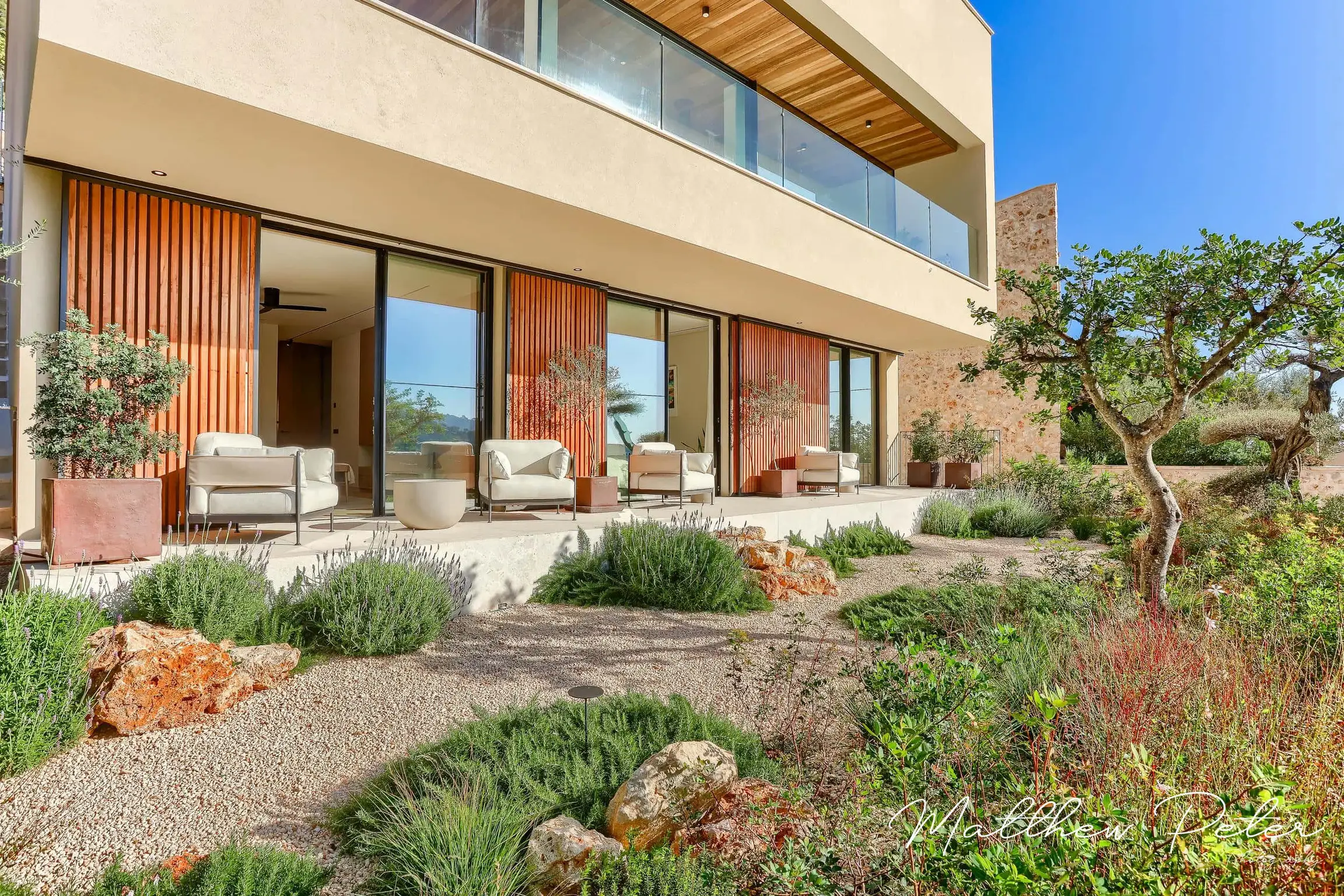 Modern villa with wide terrace and gravel garden planted with Mediterranean shrubs.