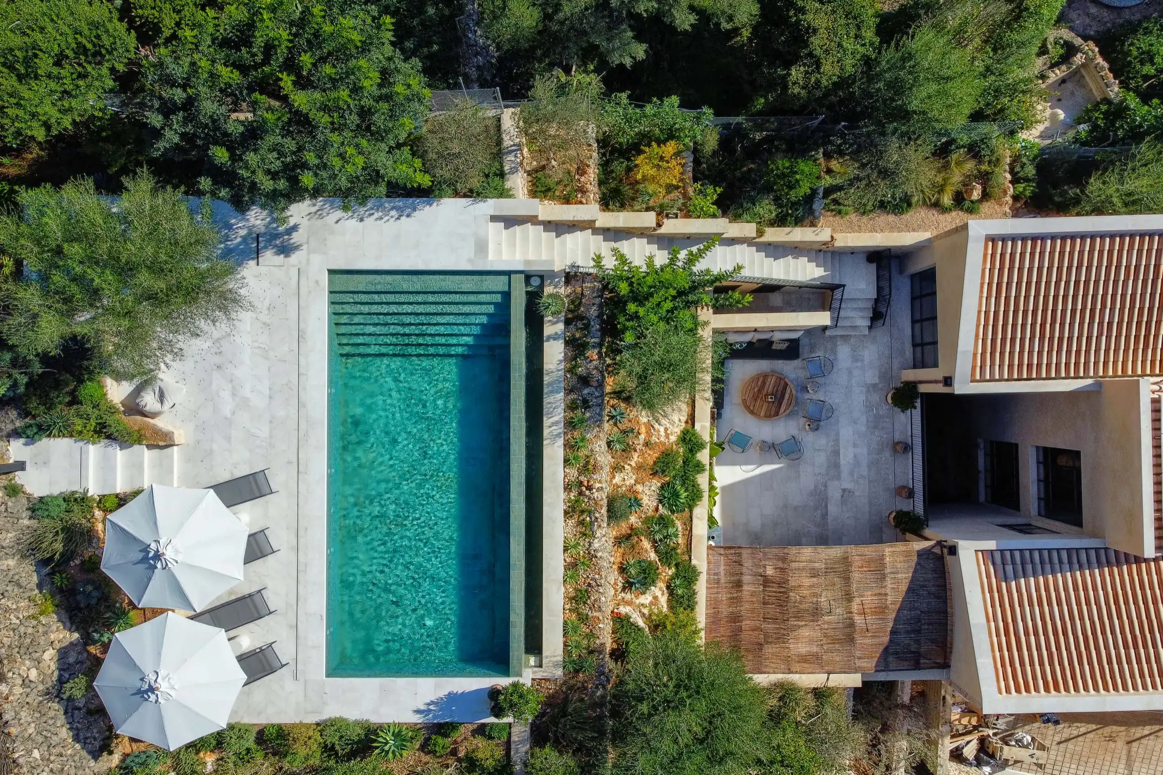 Aerial view of a rectangular pool surrounded by stone paving and lush greenery.