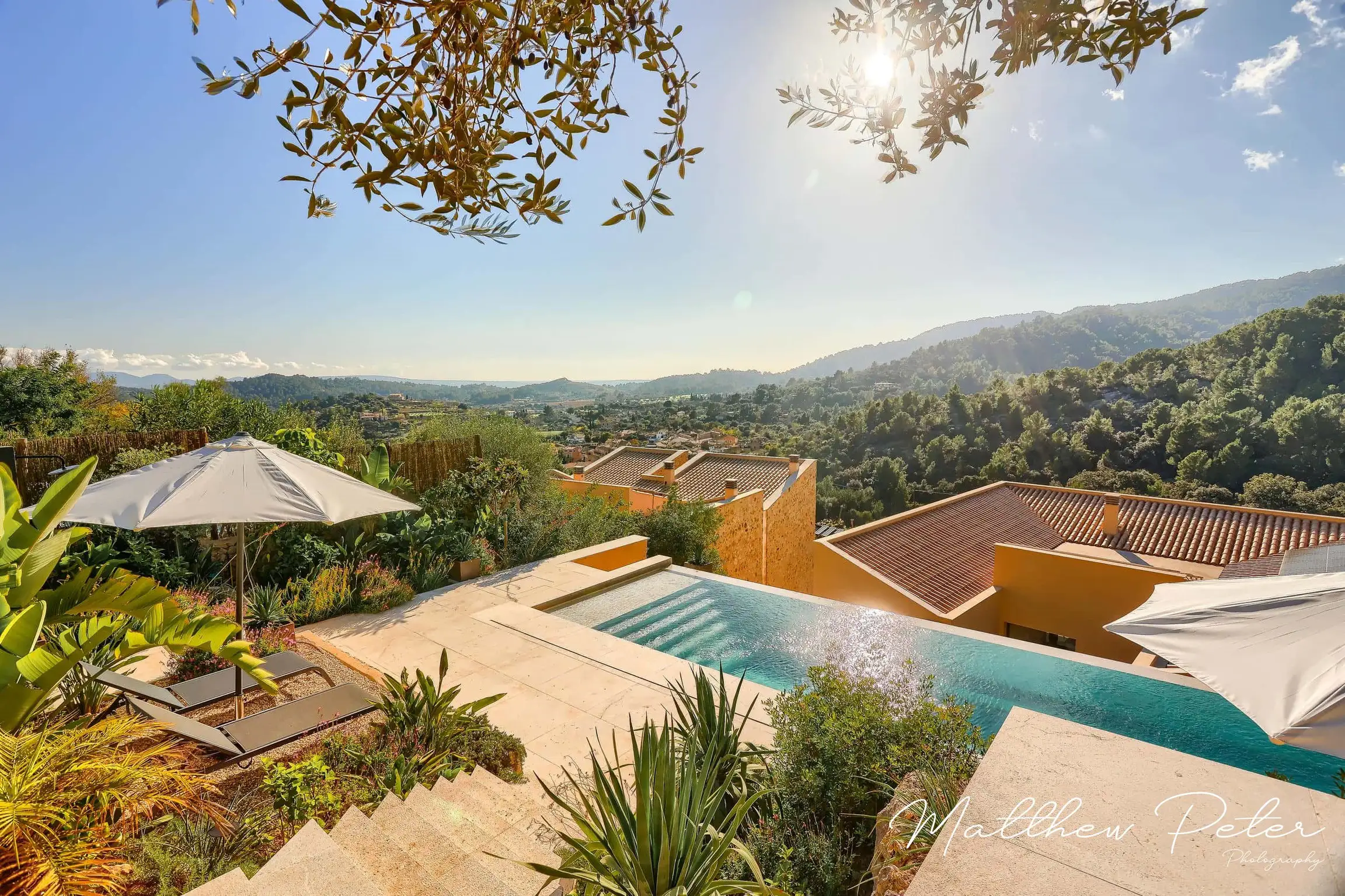 Elevated view of hillside pool terrace with panoramic landscape beyond.