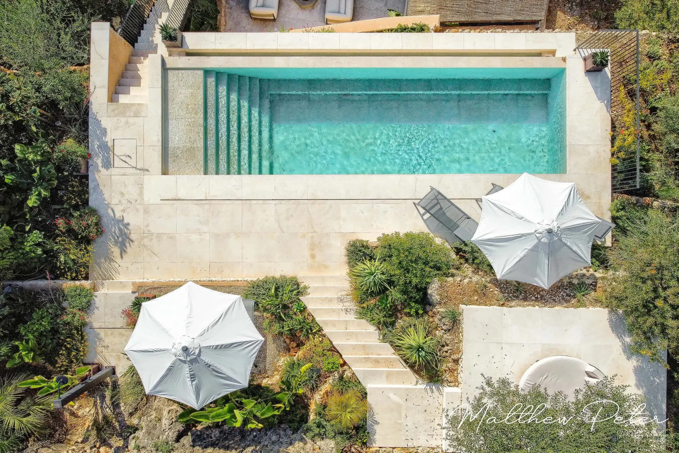 Aerial view of rectangular pool with stone steps, sun loungers, and umbrella.