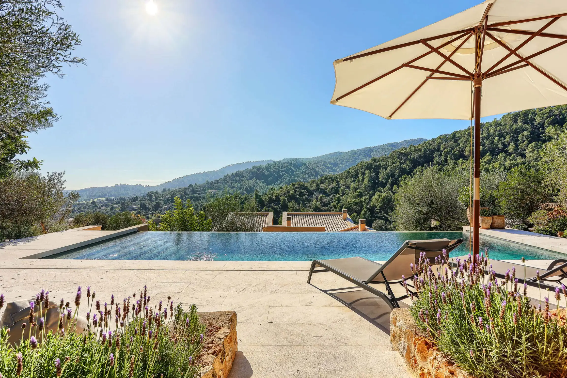 Poolside terrace with loungers, umbrella, and lavender overlooking Mallorcan hills.