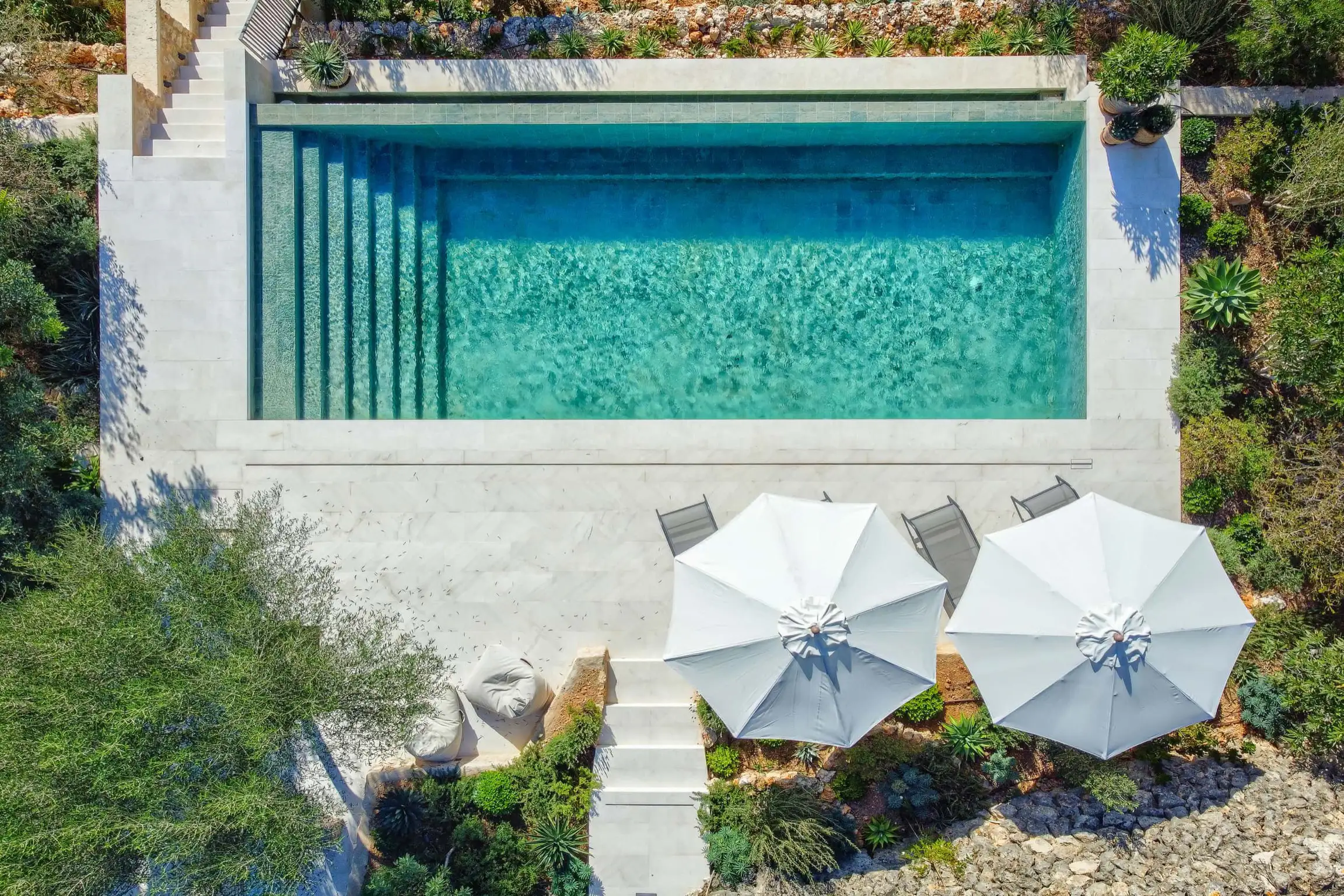 Elevated view of a turquoise pool and sun loungers with surrounding garden.