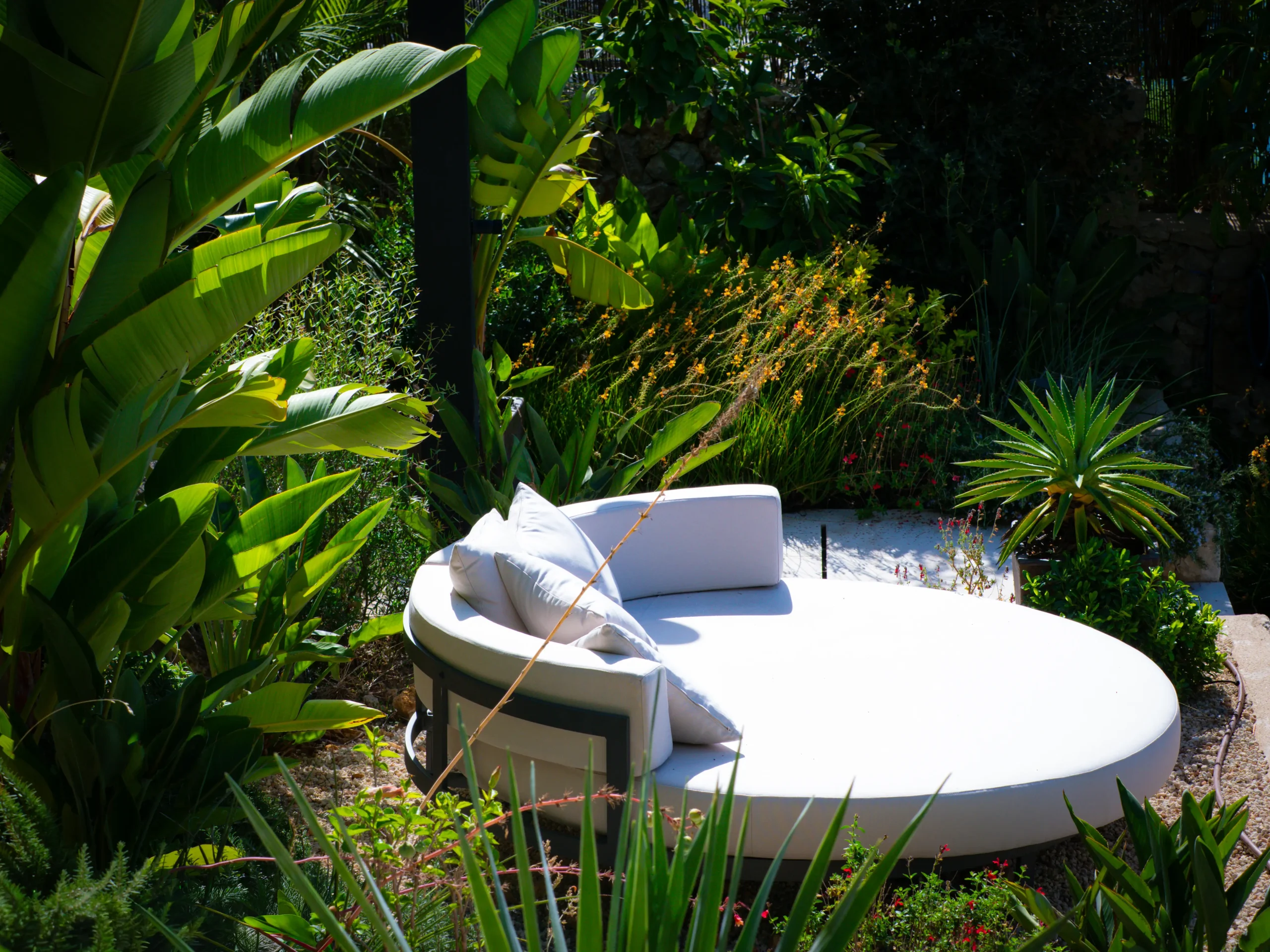 White daybed in a secluded tropical garden surrounded by dense planting.