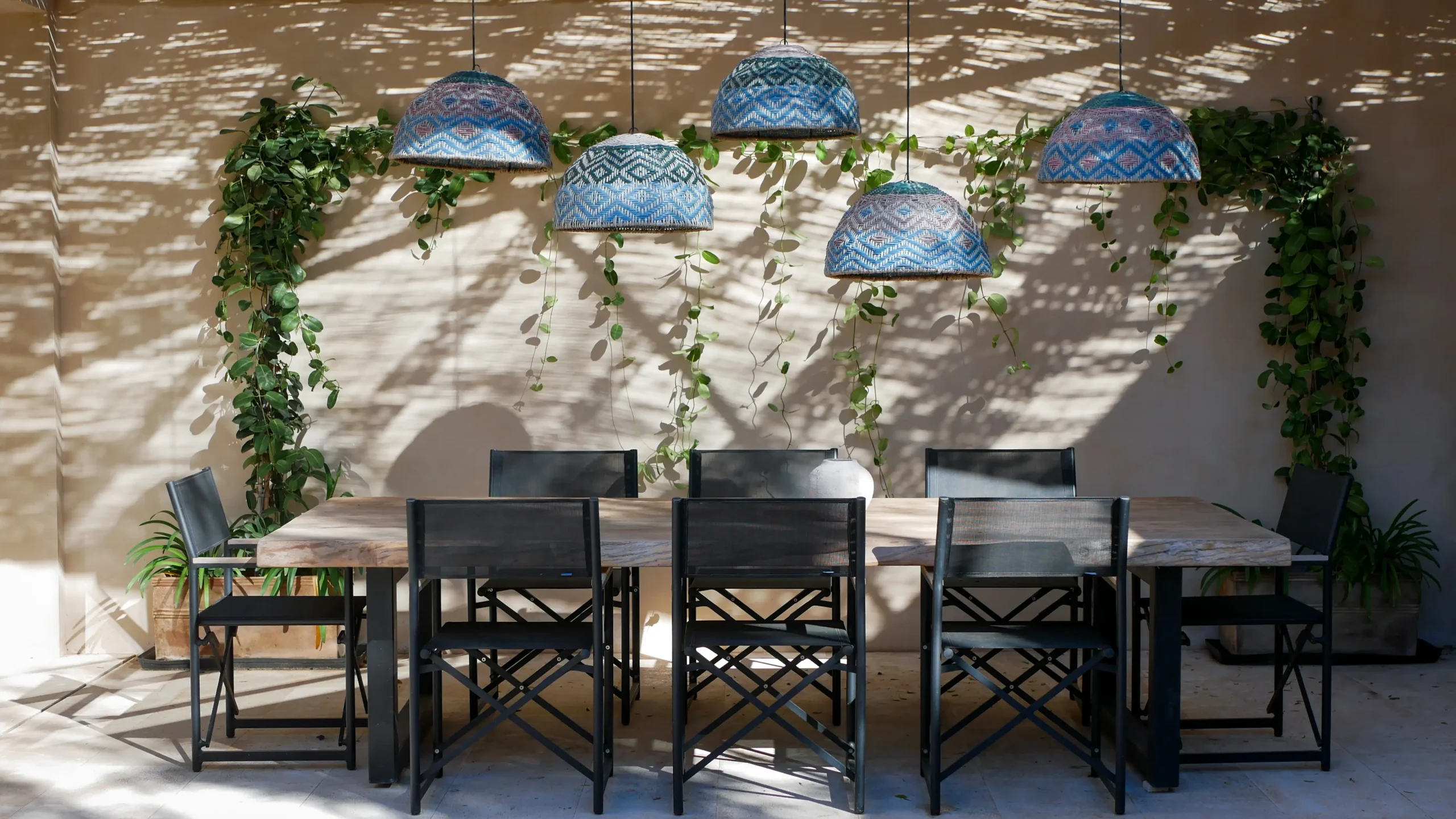 Outdoor dining area with black chairs and woven pendant lights beneath a shaded pergola.