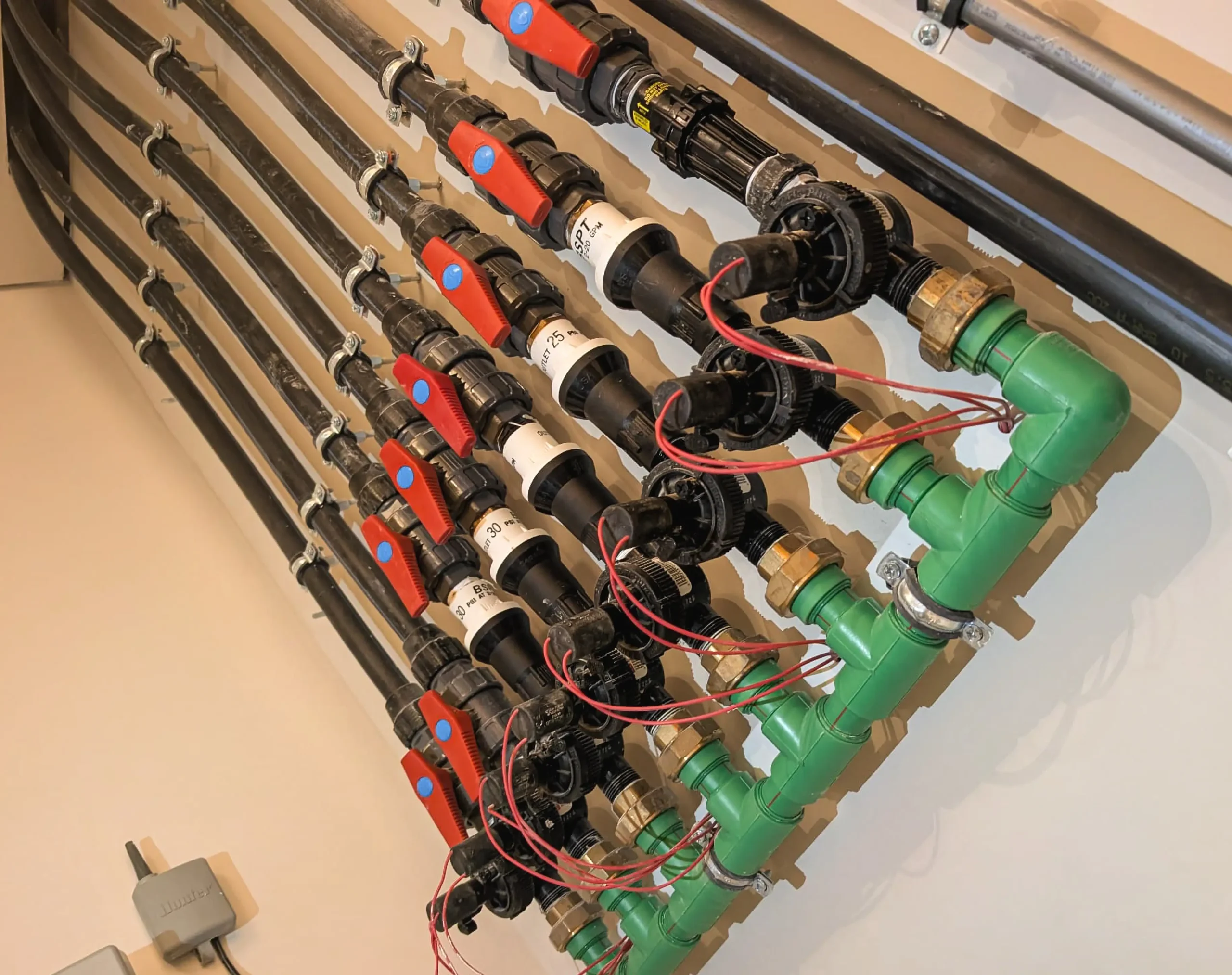 Irrigation control manifold with multiple solenoid valves, wiring, and black poly pipes for automated water distribution